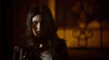 a woman in a black jacket is standing in a dark room looking at the camera .