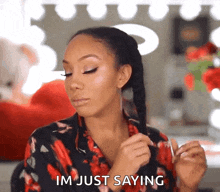 a woman in a floral shirt is holding her hair and saying im just saying