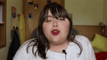 a woman wearing a white sweater and red lipstick is sitting in front of a microphone .