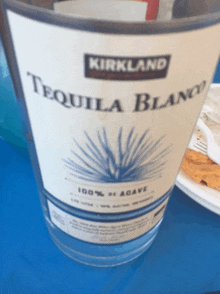 a bottle of kirkland tequila blanco sits on a table next to a plate of food