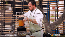 a man in an apron is using a blender in a kitchen with a shark in the background