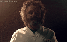 a man with curly hair and a beard is wearing a white scrub with the number 5280 on his pocket