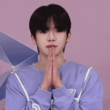 a young man in a purple sweatshirt is praying with his hands folded .