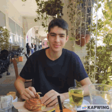 a young man is sitting at a table with a plate of food and a glass of tea with the word kapwing on the bottom