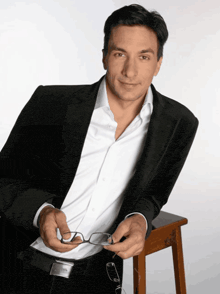 a man in a suit holds a pair of glasses in his hand