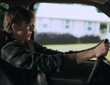 a young man is driving a car and looking out the window