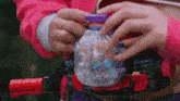 a person in a pink jacket is holding a toy with a purple container that says ' a ' on it