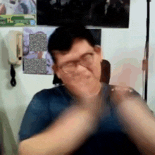 a man with glasses is clapping his hands in front of a wall with pictures on it