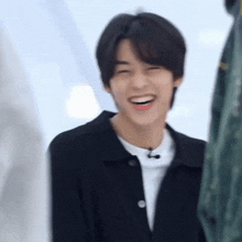 a young man in a black jacket is smiling and laughing .