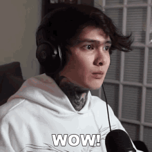 a man wearing headphones and a white shirt says wow in front of a microphone