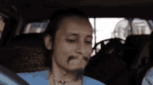 a man with a beard is sitting in a car with a steering wheel in the background