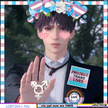 a man wearing a flower crown and a badge that says protect trans lives holds up his hand
