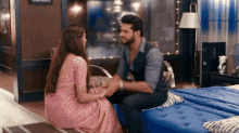 a man and a woman are sitting on a couch holding hands in a bedroom .