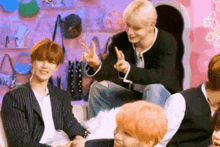 a group of young men are sitting in front of a pink wall and making peace signs .