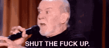 an older man is holding a microphone and saying shut the fuck up .
