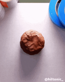 a ball of brown clay sits on a table next to a roll of blue tape