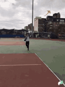 a person flying a kite on a tennis court with buildings in the background