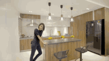 a woman is standing in a kitchen with a black refrigerator