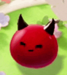 a red ball with devil horns on it is sitting on a green surface .