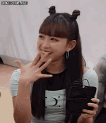 a young woman with two buns in her hair is smiling while holding a cell phone .