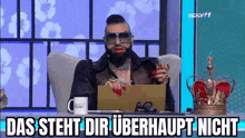 a man with a beard and red lipstick is sitting in a chair with a crown on his head .