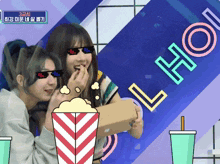 two girls wearing sunglasses are eating popcorn in front of a sign that says 3