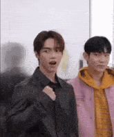 two young men are standing next to each other in a room . one of the men is wearing a pink jacket .