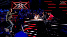 a woman sitting in a chair talking to a man on a stage with an x in the background
