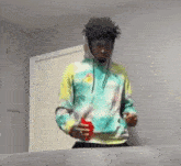 a man in a tie dye hoodie is holding a red cup and standing next to a table .