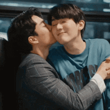 a man kissing another man on the cheek who is wearing a blue shirt that says ' a ' on it