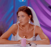 a woman in a wedding dress is sitting at a table with a pink candle in front of her
