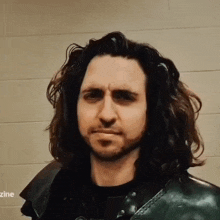 a man with long hair and a beard is wearing a black shirt and a leather jacket