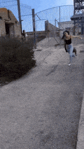 a woman is running down a street with a fence behind her and a sign that says ' ec ' on it