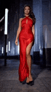 a woman in a long red dress with a high slit is walking down the street .