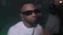 a man wearing sunglasses and a white shirt is dancing in a club .