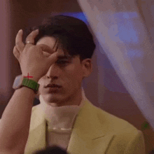 a man in a yellow suit is touching his face with his hand .