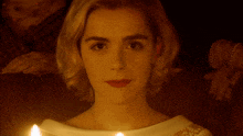 a close up of a woman 's face with candles behind her