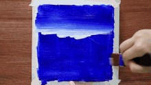 a person is painting a blue square on a wooden surface