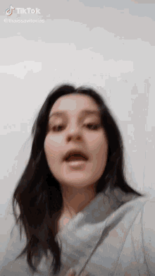 a woman with long dark hair is making a funny face in a tik tok video .