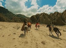 a group of people riding horses in the desert with mountains in the background