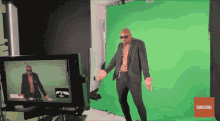 a man in a suit is standing in front of a green screen with a subscribe button