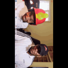 a man wearing an adidas shirt is standing next to another man wearing a red hard hat