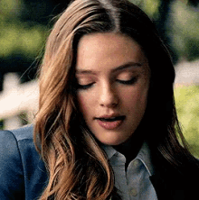 a woman with long hair is wearing a blue jacket and white shirt .