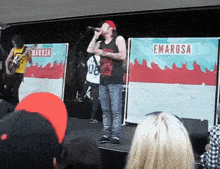 a man singing into a microphone in front of emarosa posters