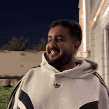 a man wearing a white adidas hoodie smiles for the camera