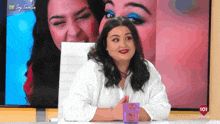 a woman sits in front of a tv screen that says sevilla 101