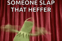 kermit the frog is standing in front of a red curtain with the words `` someone slap that heffer '' written on it .