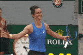 a woman in a blue tank top is holding a tennis racquet in front of a rolex sign