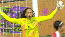 a female soccer goalie wearing a snapdragon jersey holds her arms up in the air .