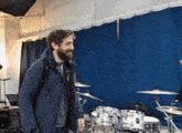 a man in a blue jacket stands in front of a drum set with a cymbal that says bb on it